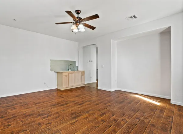 a view of an empty room with wooden floor and a ceiling fan