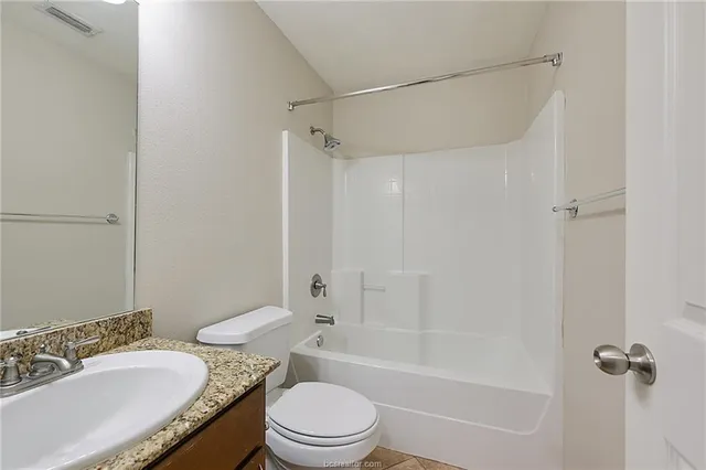 a bathroom with a granite countertop bathtub shower sink vanity mirror and toilet