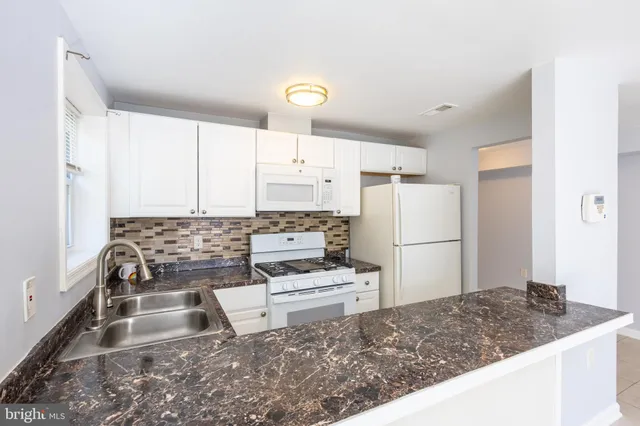 a kitchen with kitchen island granite countertop a sink a stove a refrigerator and white cabinets