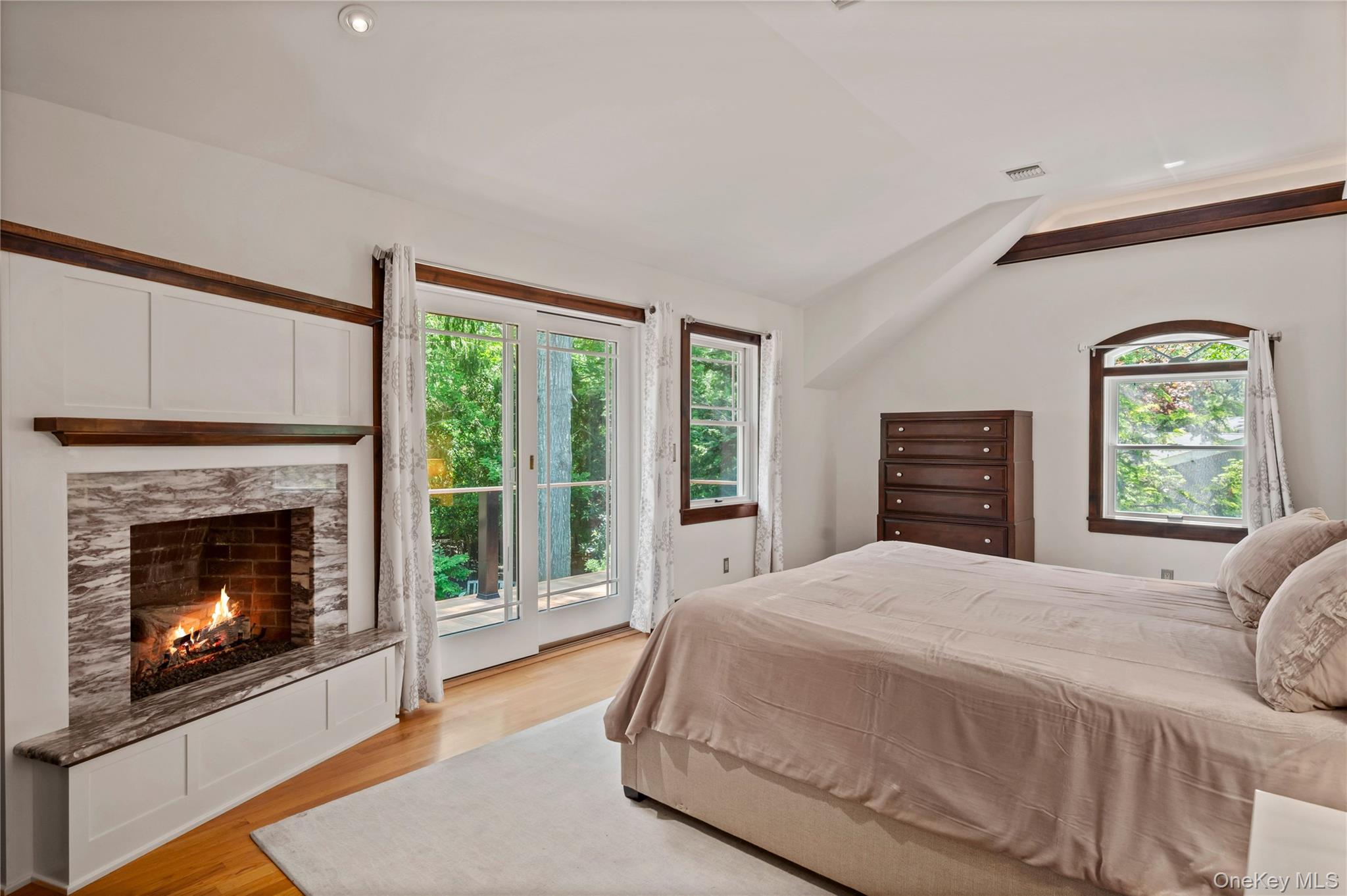 4745 North Bayview Road Southold, NY 11971 - Photo 13 of 31 Bedroom featuring access to exterior, multiple windows, a warm lit fireplace, light wood-style flooring, and vaulted ceiling