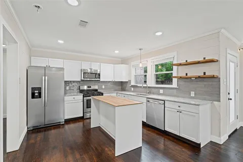 a kitchen with stainless steel appliances a stove a sink dishwasher a refrigerator and white cabinets with wooden floor