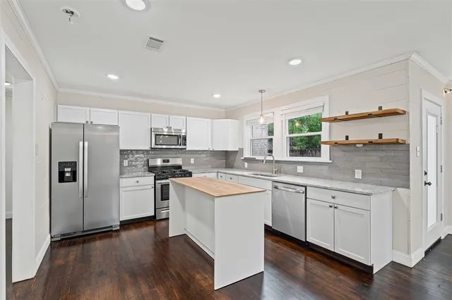 a kitchen with stainless steel appliances a stove a sink dishwasher a refrigerator and white cabinets with wooden floor