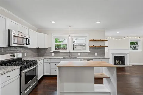 a kitchen with stainless steel appliances granite countertop a stove top oven a sink dishwasher and a refrigerator with wooden floor