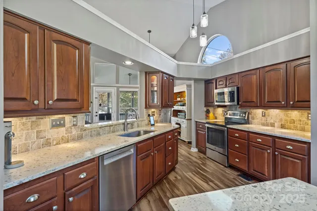 a kitchen with stainless steel appliances granite countertop wooden cabinets a sink dishwasher a stove and a refrigerator with wooden cabinets