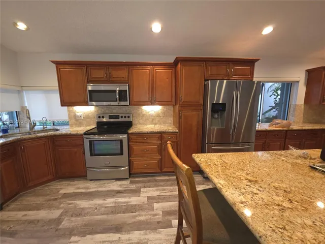 a kitchen with stainless steel appliances kitchen island granite countertop a refrigerator stove and sink