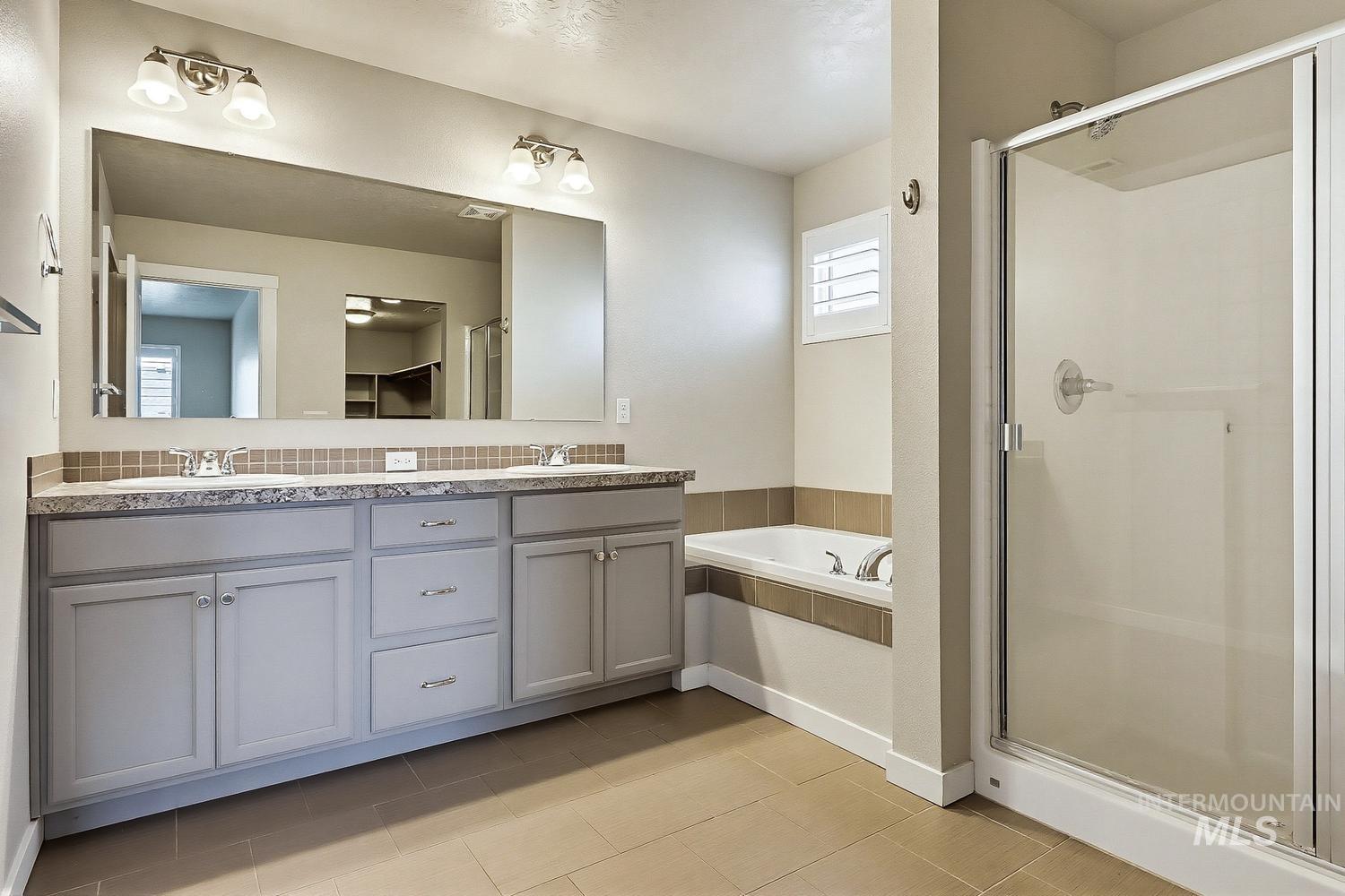 846 North Hidden View Way Star, ID 83669 - Photo 34 of 49 Spacious bathroom featuring a dual vanity with light gray cabinetry and a stone-finish countertop, a large frameless mirror, a built-in tub with tile surround, and a glass-enclosed shower