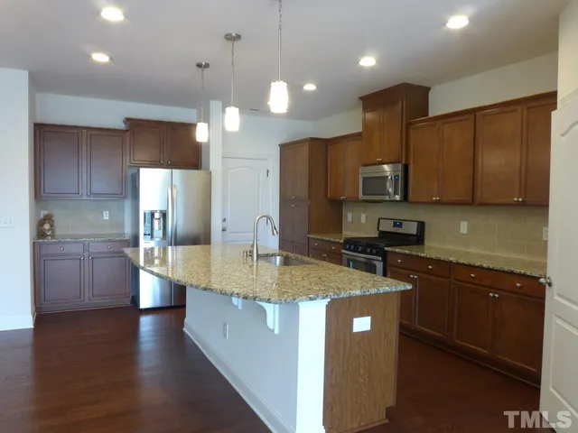 a kitchen with stainless steel appliances granite countertop a sink a stove a refrigerator a center island and a wooden floor