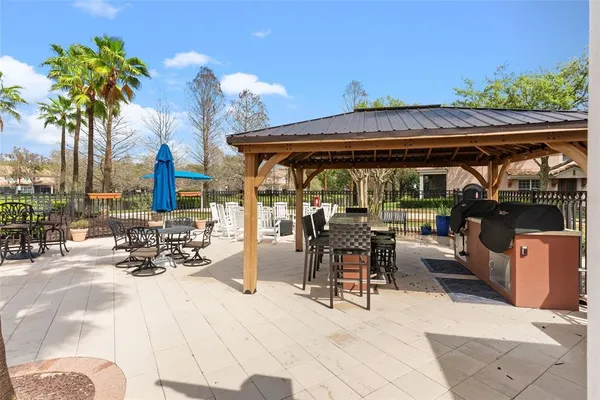 a view of a patio with dining table and chairs under an umbrella with a barbeque grill and plants