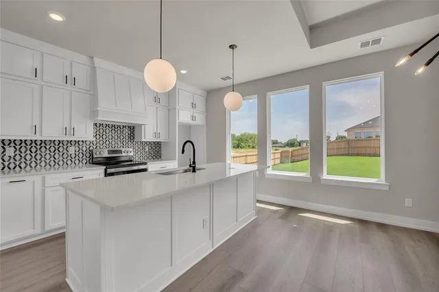 a open kitchen with granite countertop a stove top oven a sink and white cabinets with wooden floor