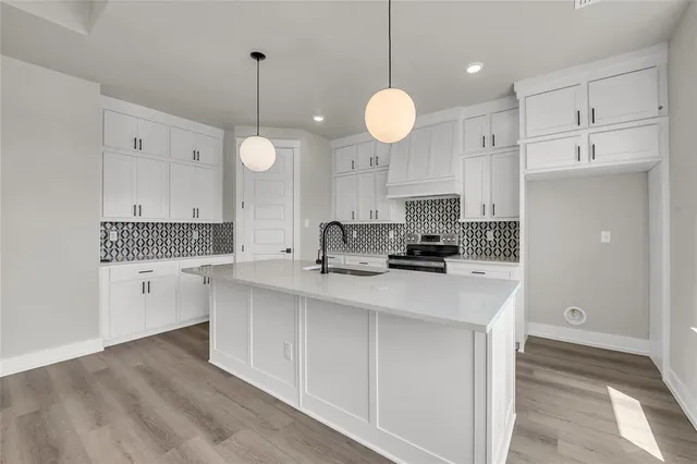 a large white kitchen with granite countertop a stove a sink and white cabinets with wooden floor