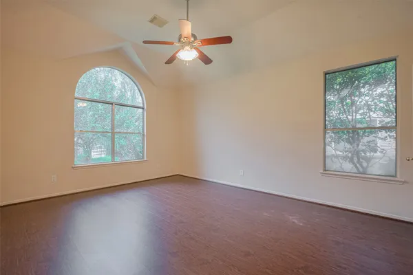 an empty room with wooden floor chandelier fan and windows