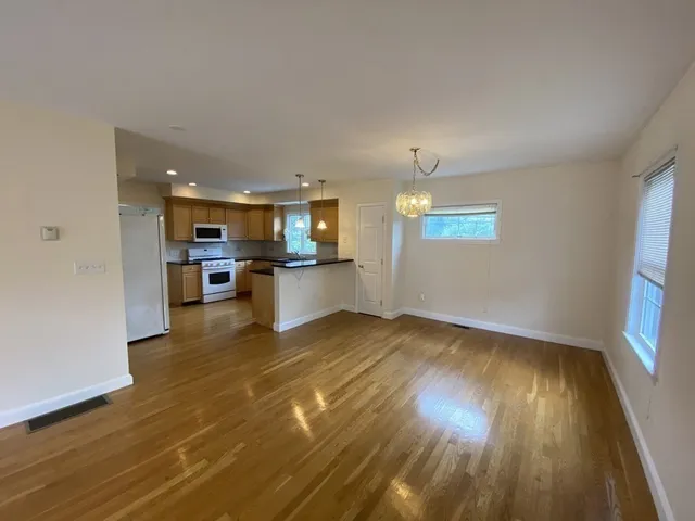 a view of a kitchen and an empty room with wooden floor and a kitchen