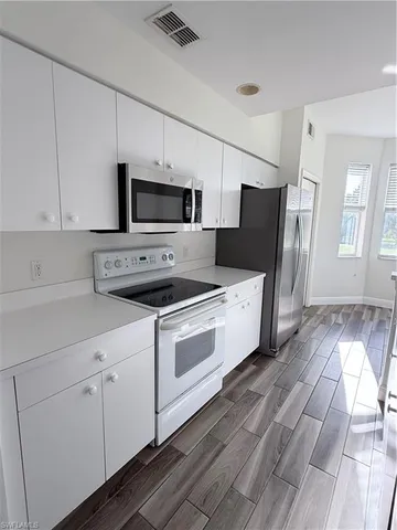 a kitchen with stainless steel appliances white cabinets a sink a stove a microwave and wooden floors