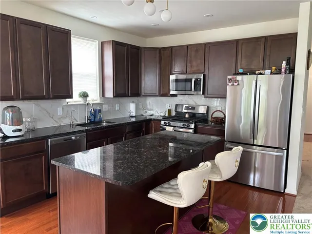 a kitchen with granite countertop stainless steel appliances a sink a refrigerator a stove a dining table and chairs