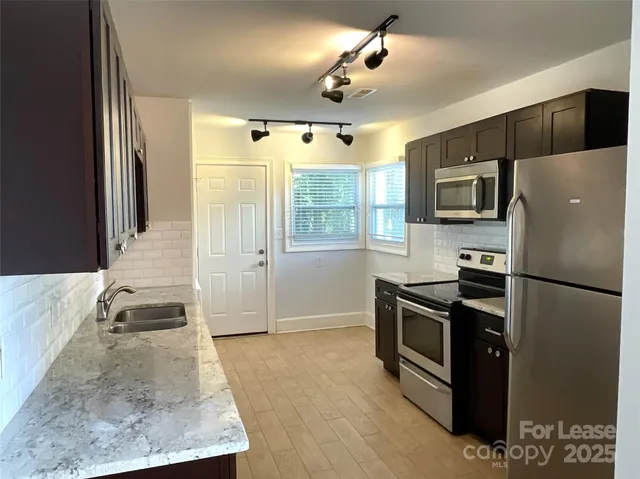 a kitchen with stainless steel appliances granite countertop a refrigerator a stove and a sink with wooden floor