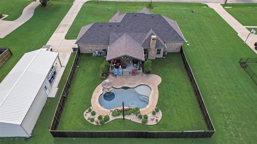 Fenced backyard featuring a freeform swimming pool with a sun shelf and water feature, surrounded by mature landscaping