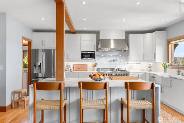a kitchen with stainless steel appliances kitchen island granite countertop a stove a refrigerator a dining table and chairs with wooden floor