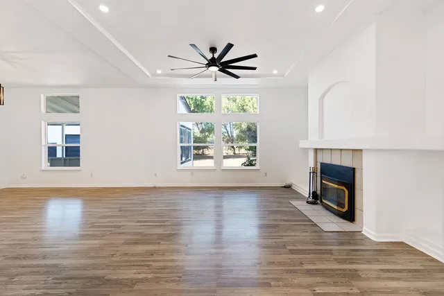 a view of a livingroom with a hardwood floor a ceiling fan and windows