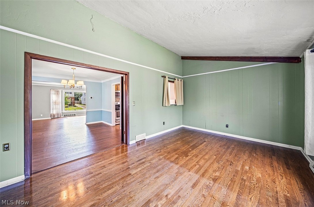 4069 Bushnell Road Cleveland, OH 44121 - Photo 12 of 39 Spare room with a chandelier, dark wood finished floors, vaulted ceiling, and wooden walls
