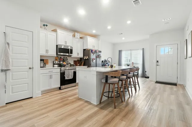 a kitchen with kitchen island wooden floors appliances and white cabinets
