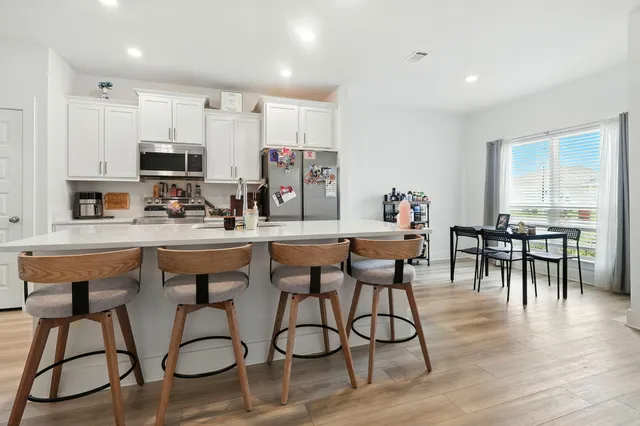 a kitchen with stainless steel appliances kitchen island granite countertop a stove a refrigerator a sink a dining table and chairs with wooden floor