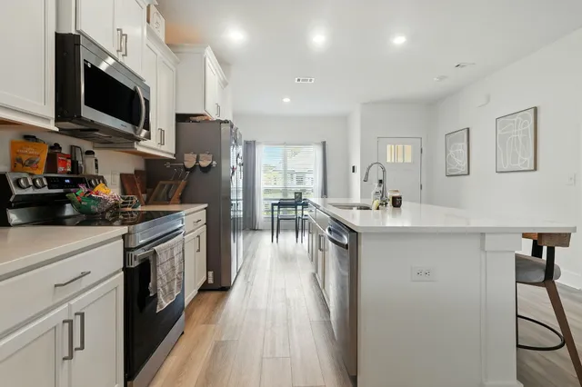 a kitchen with stainless steel appliances granite countertop a refrigerator a stove top oven a sink dishwasher and white cabinets with wooden floor