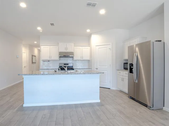 a kitchen with stainless steel appliances granite countertop a refrigerator a sink a stove and white cabinets with wooden floor