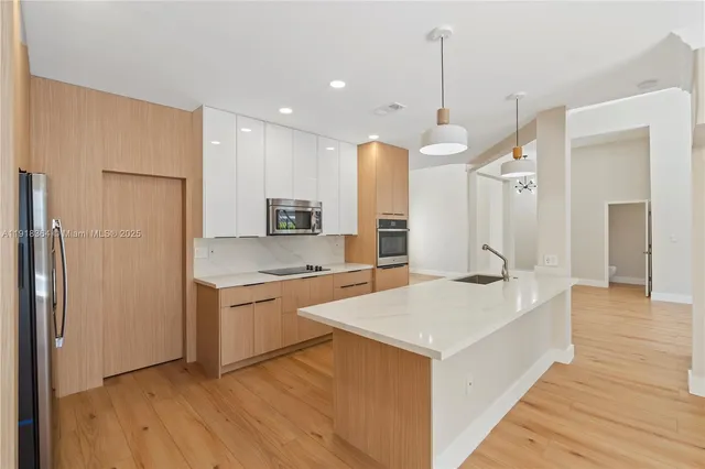 a large kitchen with kitchen island a sink dishwasher a refrigerator and white cabinets next to a window