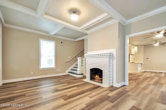 a view of an empty room with wooden floor fireplace and a window