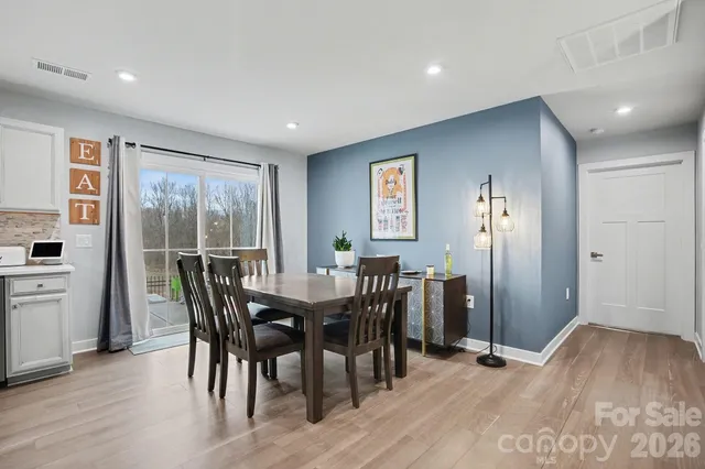 a large kitchen with stainless steel appliances a stove a sink dishwasher a refrigerator white cabinets a dining table and chairs with wooden floor