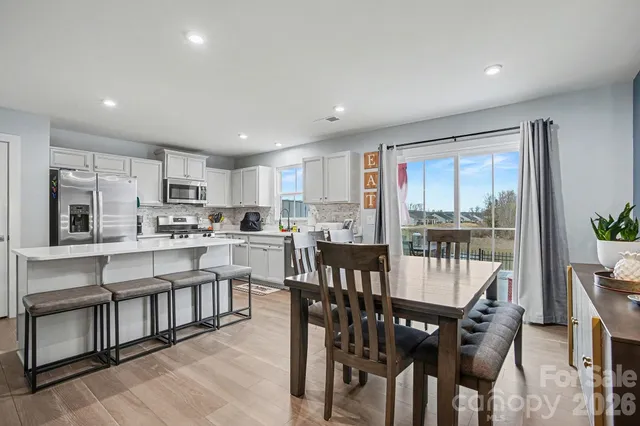 a kitchen with stainless steel appliances kitchen island granite countertop a refrigerator a stove a sink a dining table and chairs with wooden floor