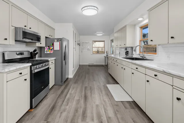 a kitchen with stainless steel appliances kitchen island granite countertop a stove top oven a sink dishwasher and a refrigerator with wooden floor