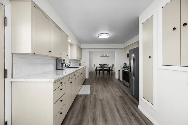 a kitchen with granite countertop a refrigerator a sink dishwasher a stove and white cabinets with wooden floor