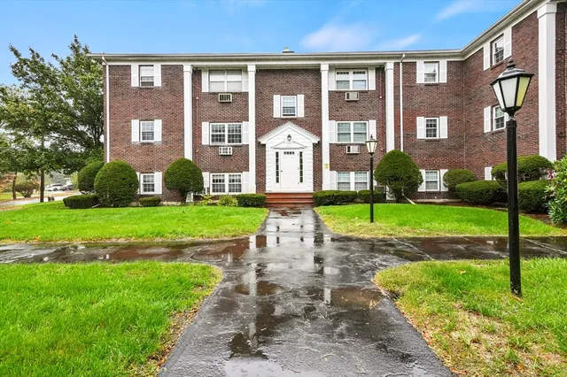 a view of a brick building next to a yard and large trees