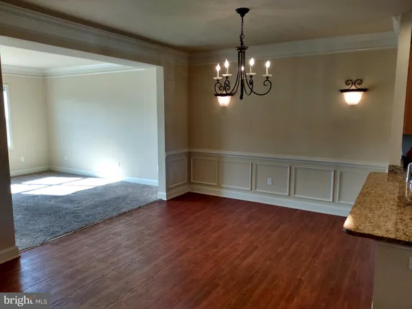 a view of empty room with wooden floor and kitchen view