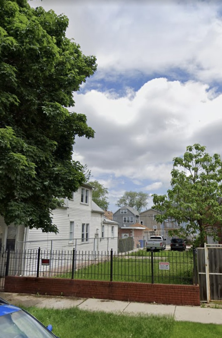 a view of a white house in front of a yard with plants and large trees