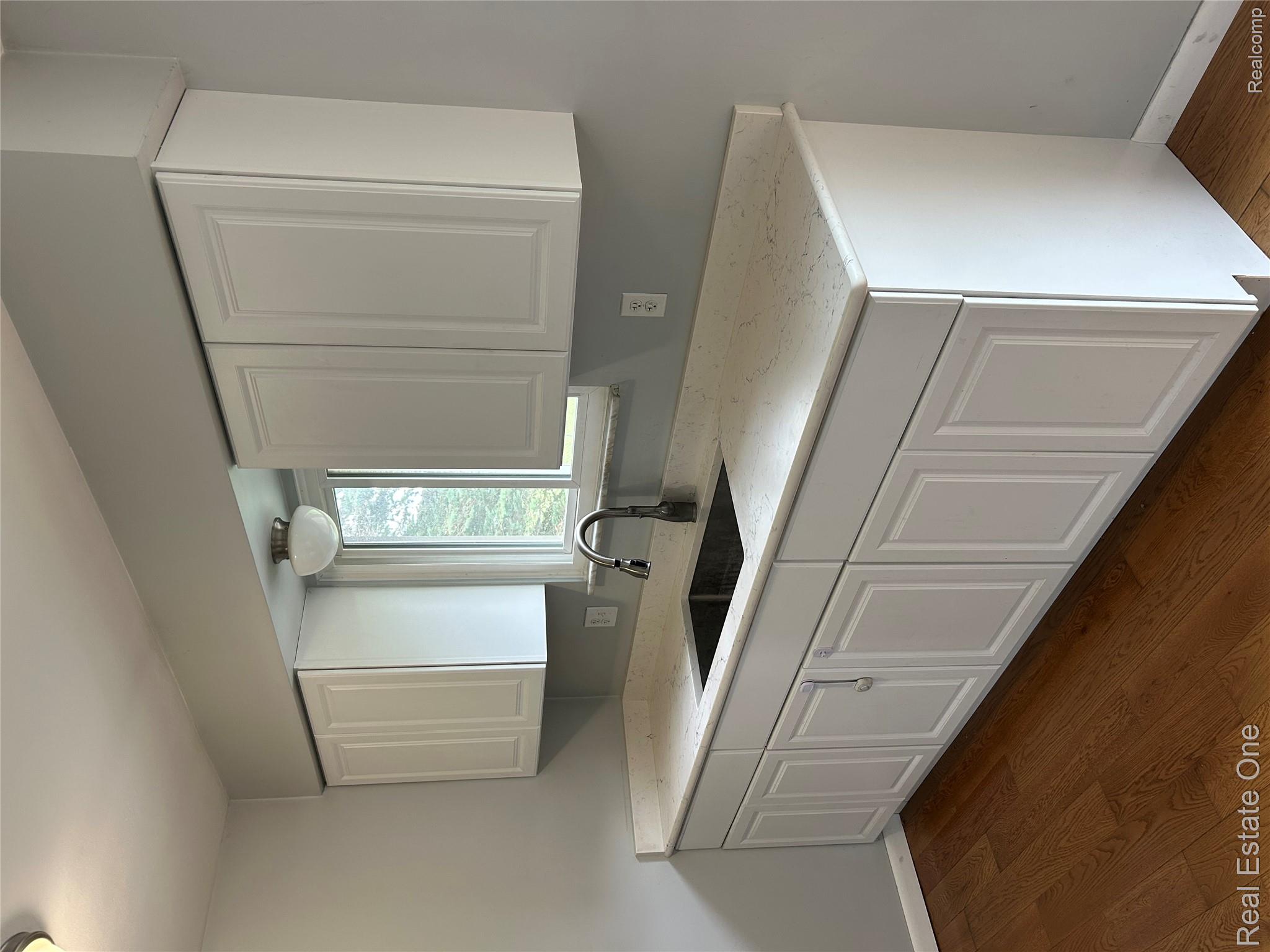 2659 Benstein Road Commerce Township, MI 48382 - Photo 5 of 26 Contemporary kitchen sink area featuring white shaker-style cabinetry, a dark basin sink with a matte black faucet, light-toned countertop, and wood-finish flooring