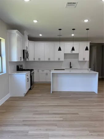 a large white kitchen with wooden floors and stainless steel appliances
