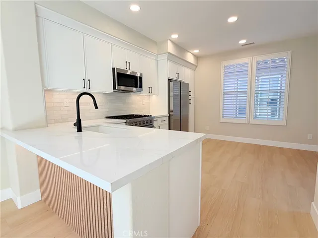 a kitchen with stainless steel appliances a sink a microwave a refrigerator and white cabinets with wooden floor