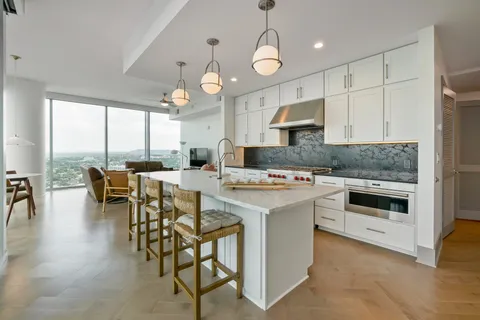 a kitchen with stainless steel appliances a stove a sink a microwave a dining table and chairs with wooden floor