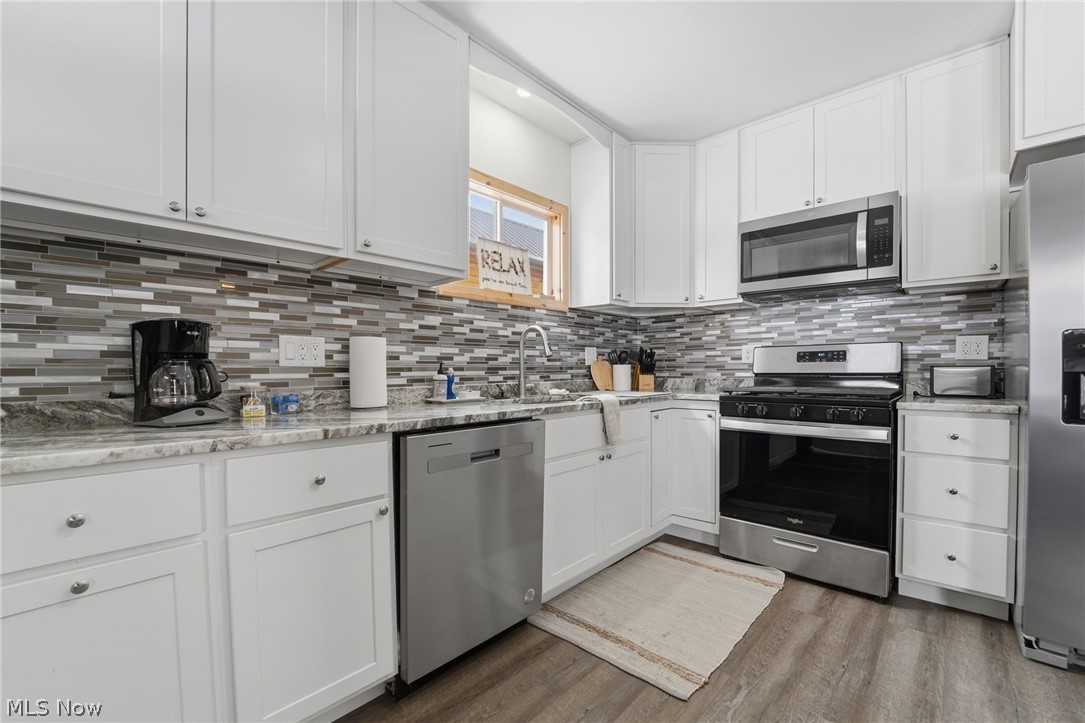 5919 Lake Road West, Unit 32 Ashtabula, OH 44004 - Photo 3 of 23 Kitchen with white cabinets, stainless steel appliances, light stone counters, light wood-style flooring, and decorative backsplash