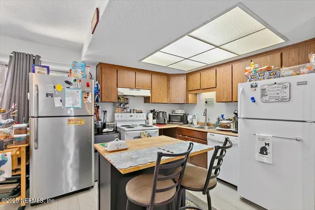 a kitchen with granite countertop a refrigerator a sink a stove and chairs with wooden floor