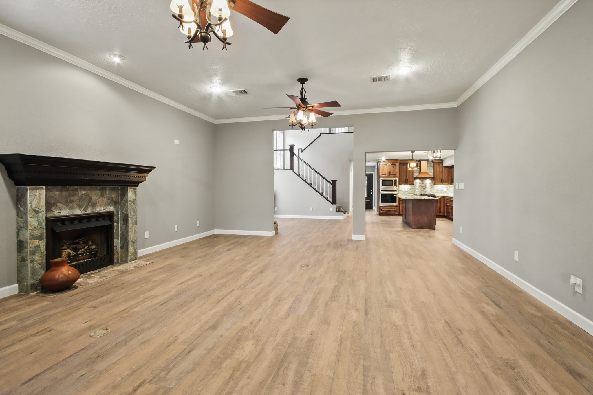 35 Susan Drive Cleveland, TX 77327 - Photo 6 of 33 Spacious open-concept living area featuring a cozy fireplace, elegant chandeliers, and warm flooring. The room seamlessly connects to a modern kitchen with a central island and stainless steel appliances, complemented by a view of the stylish staircase.