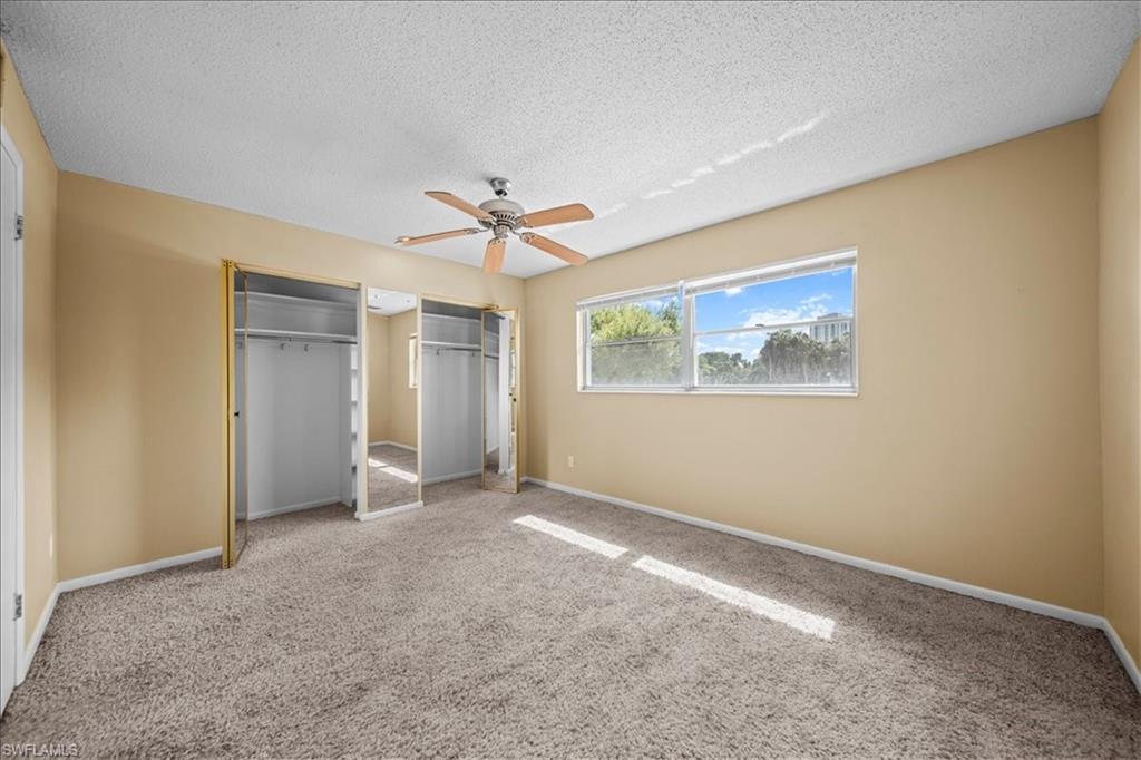 3225 East Riverside Drive, Unit 17A Fort Myers, FL 33916 - Photo 15 of 30 Unfurnished bedroom with two closets, carpet flooring, a ceiling fan, and a textured ceiling