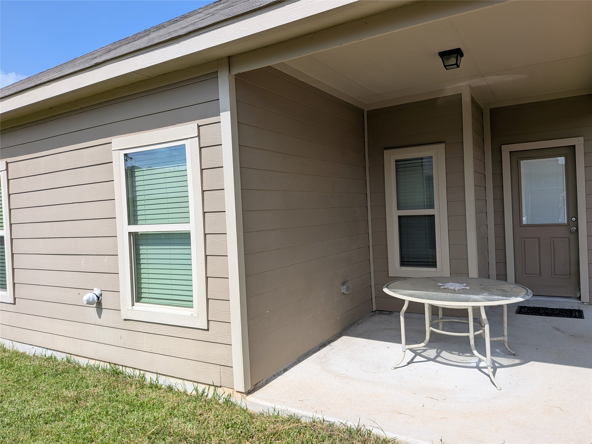 15730 Joe Dimaggio Street Splendora, TX 77372 - Photo 20 of 20 Cozy back patio area with a small table, sheltered by a roof overhang. The space is adjacent to the home's exterior, featuring two windows and a door, perfect for outdoor relaxation.