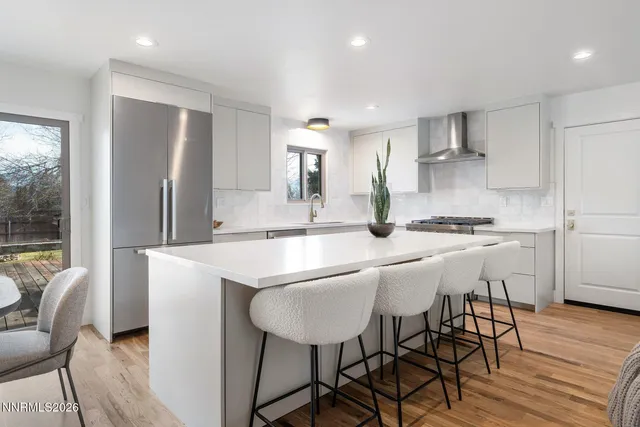 a kitchen with stainless steel appliances granite countertop a stove a refrigerator a sink a dining table and chairs with wooden floor