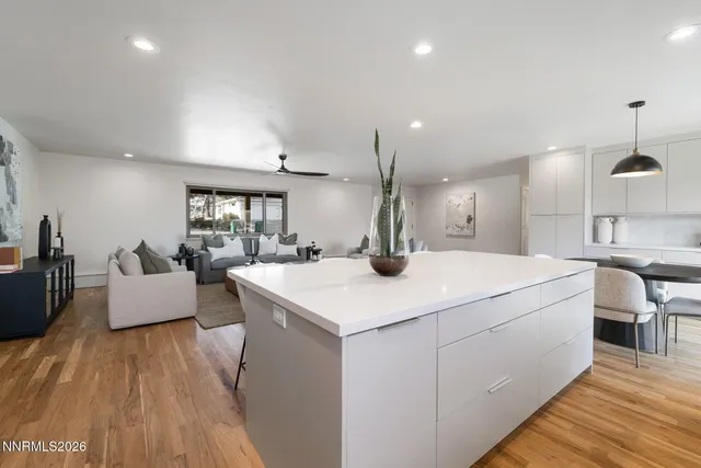 a large white kitchen with a white countertops a couch and a dining table with wooden floor