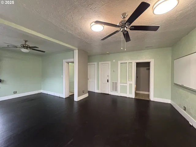 an empty room with wooden floor fan and windows