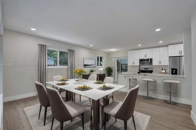 a dining room with stainless steel appliances kitchen island granite countertop a dining table chairs and a refrigerator