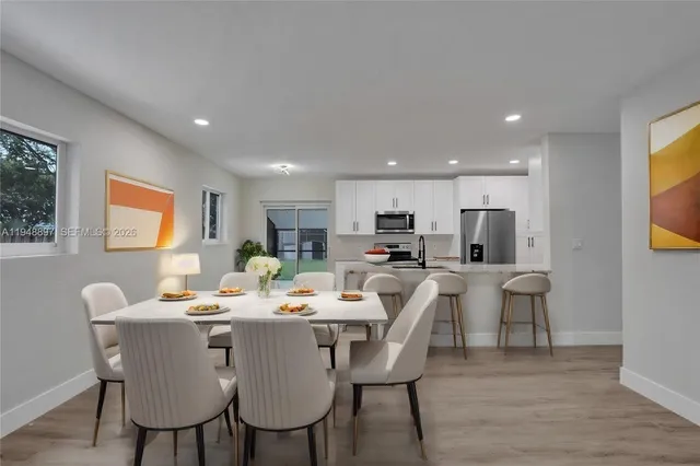 a dining room with stainless steel appliances kitchen island granite countertop a dining table chairs and a refrigerator